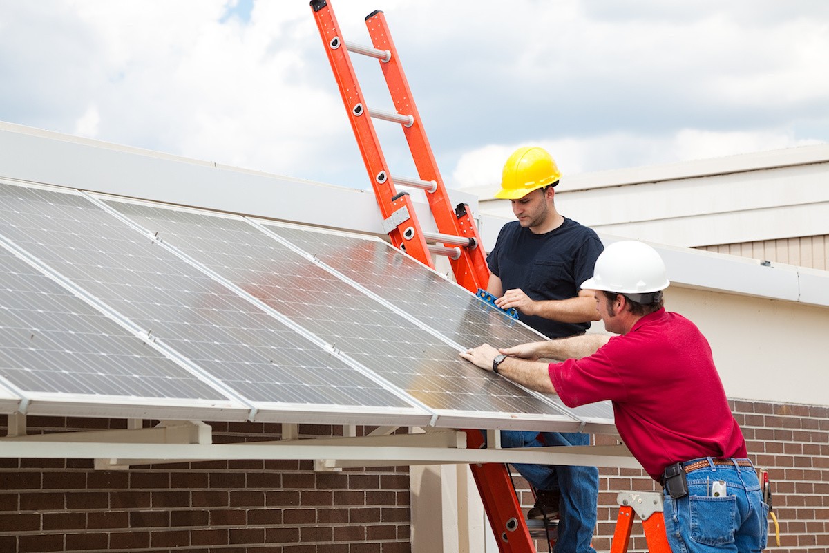 two men in hard hats installing solar panels to a building