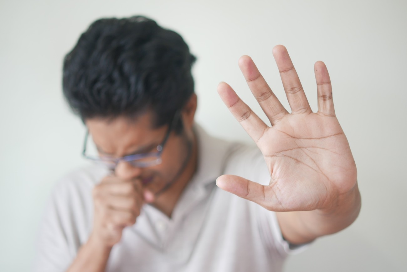 man coughing and holding his hand in front of his face